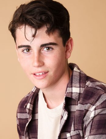 Headshot of a young adult male with brown hair wearing a plaid shirt against a neutral background in a studio setting. 