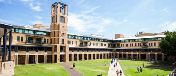 Exterior courtyard of a brick education building with a clock tower and students walking on green grass paths.
