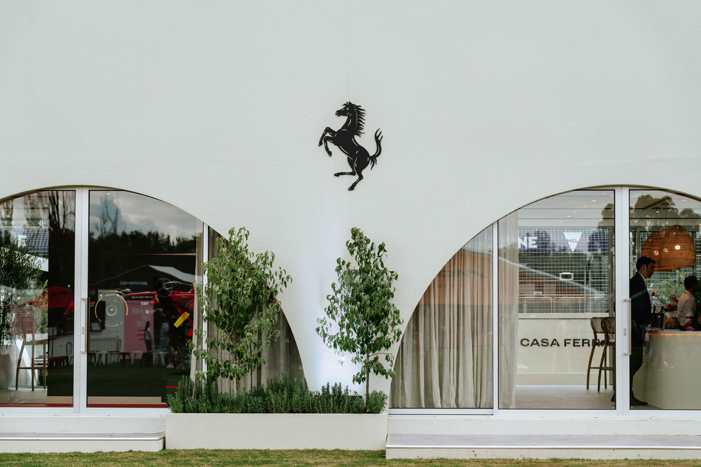 Exterior view of Casa Ferrari with a black prancing horse logo above arching windows and greenery, showcasing a blend of automotive and design.