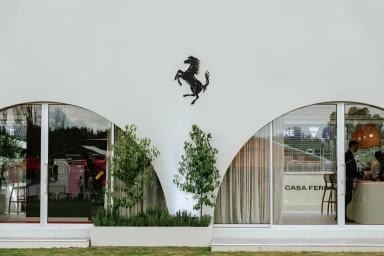 Exterior view of a white building with arched windows, a black rearing horse emblem, and planters with small trees by Bastion Creative