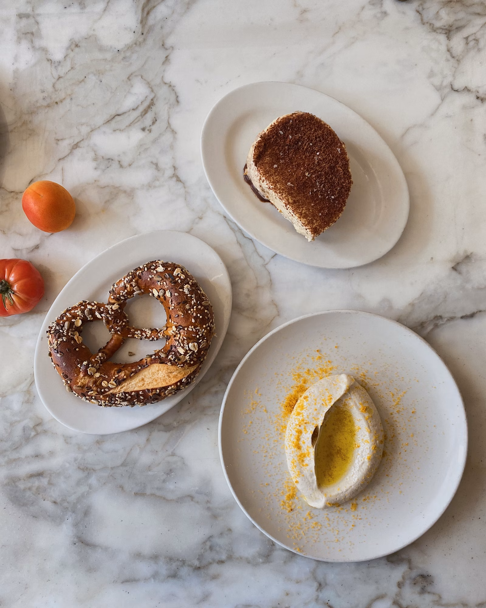 Overhead shot of a pretzel, a sweet pastry, and a dip arranged on plates, displayed on a marble surface.