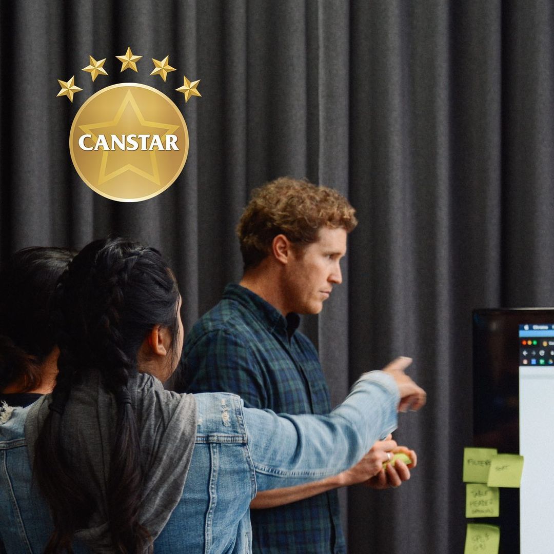 Two women and a man collaborating on a project, with one man pointing at a screen and sticky notes attached to the monitor.