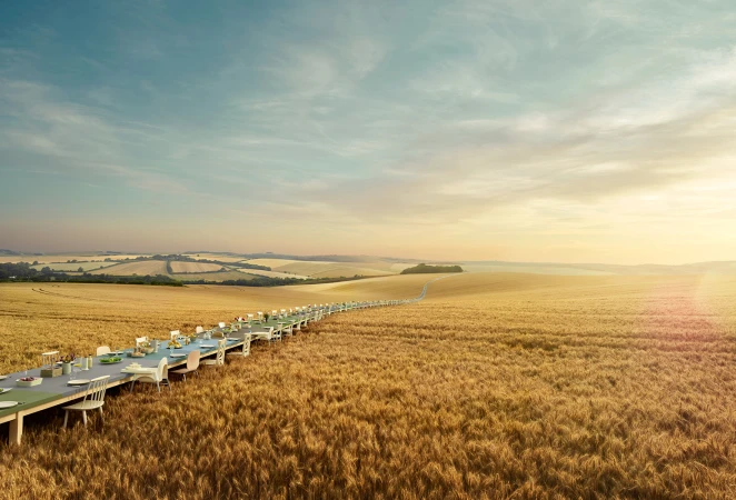 A surreal outdoor dining experience features an extremely long table set in a golden field under a blue sky, creating a dreamlike atmosphere.