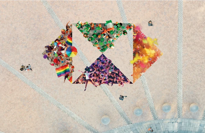 Overhead view of groups of people in a public square, arranged into geometric shapes with rainbow flags, green balloons, and colored powder.