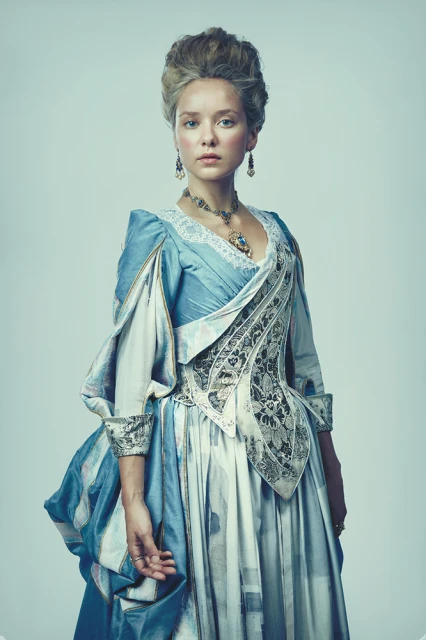 Elegant portrait of a young woman in an ornate blue dress with puffed sleeves and lace details, posing in a photo studio setting.