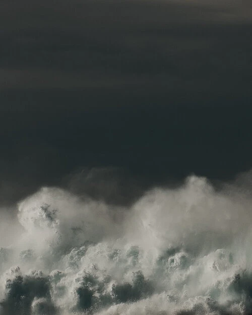 A dynamic cloudscape shows turbulent white clouds against a dark grey sky, creating a dramatic natural scene with a sense of scale.