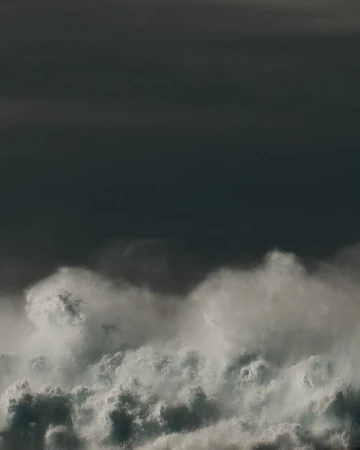 A dynamic cloudscape shows turbulent white clouds against a dark grey sky, creating a dramatic natural scene with a sense of scale.