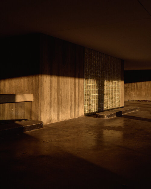 Concrete architecture interior with glass block wall illuminated by light in a shadowed, minimalist architectural composition.