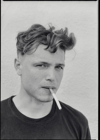 Monochrome portrait of a young adult man with styled hair, smoking a cigarette against a plain white background in a close-up shot.