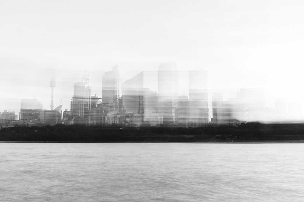 Monochrome cityscape view of a city skyline featuring high-rise buildings, water, and land under an overcast sky, creating a tranquil scene.