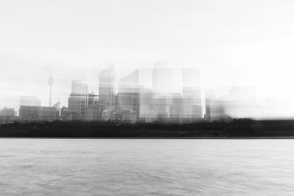 Monochrome cityscape view of a city skyline featuring high-rise buildings, water, and land under an overcast sky, creating a tranquil scene.
