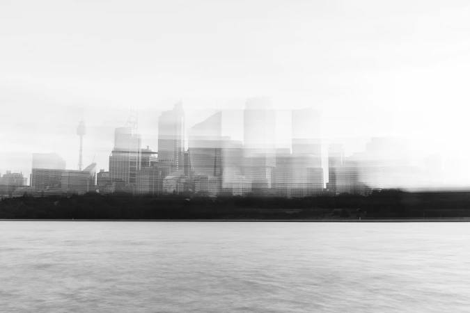 Monochrome cityscape view of a city skyline featuring high-rise buildings, water, and land under an overcast sky, creating a tranquil scene.