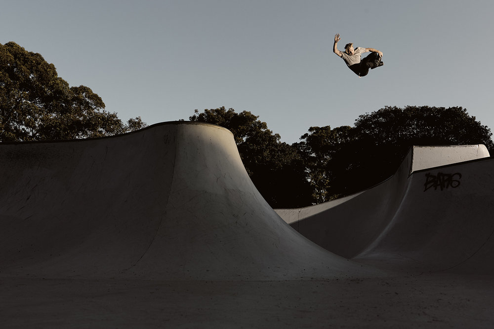 A solo skateboarder catches air over a concrete ramp in an outdoor skatepark against a clear sky, showcasing athleticism.