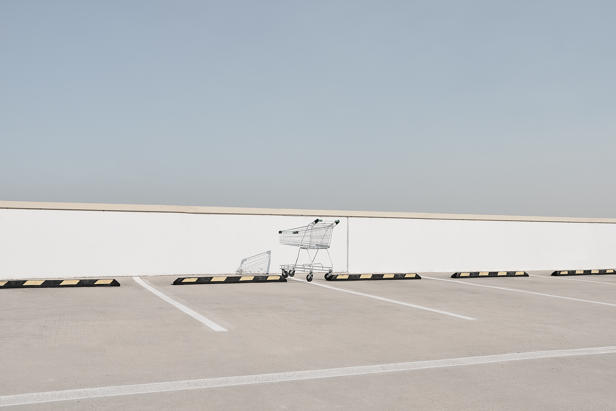 Abandoned shopping cart and goal on an empty outdoor parking lot under a light blue sky. Minimalist and desolate.