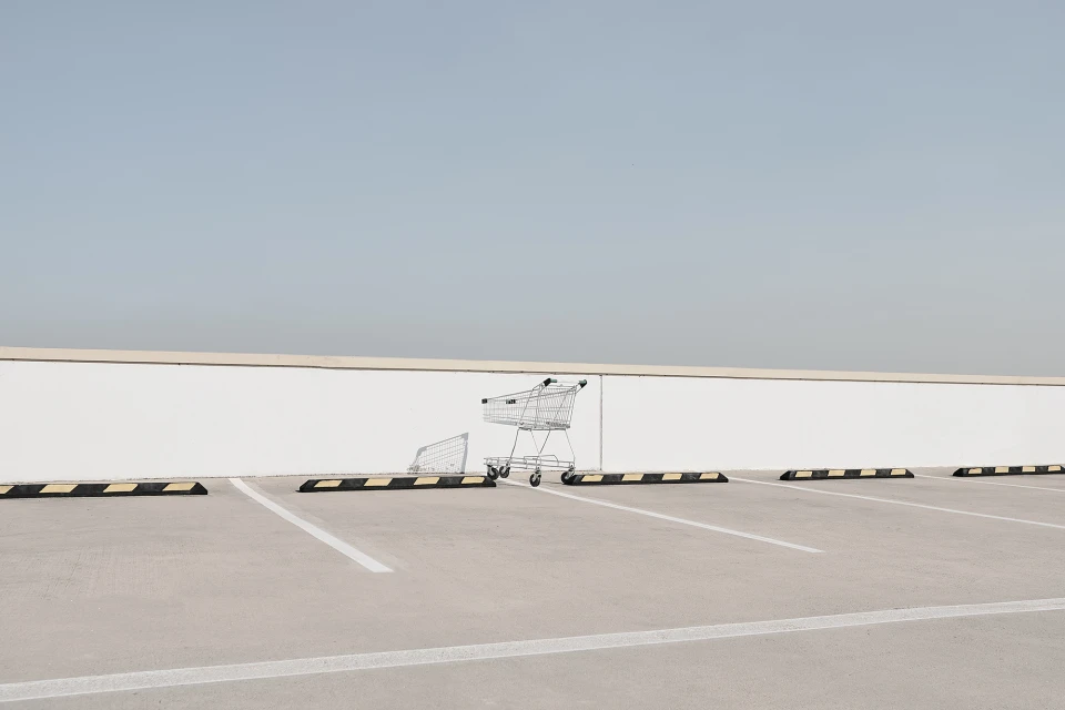 Abandoned shopping cart and goal on an empty outdoor parking lot under a light blue sky. Minimalist and desolate.