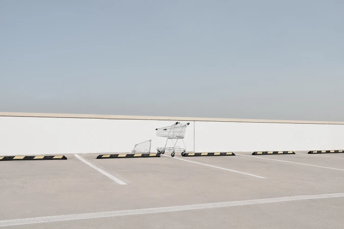 Abandoned shopping cart and goal on an empty outdoor parking lot under a light blue sky. Minimalist and desolate.