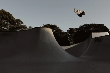 Skater performing an aerial trick above a concrete skatepark bowl against a clear sky