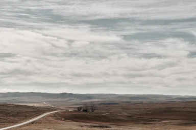 Wide landscape photography showing a vast flat terrain under a heavy, overcast cloudy sky with a winding road.
