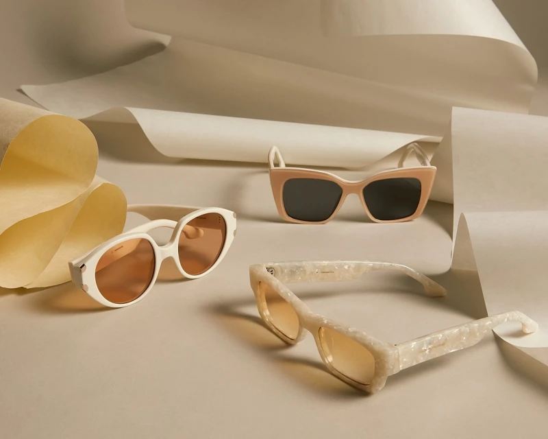 Three pairs of sunglasses are displayed against a neutral backdrop with gently curving white paper, showcasing fashion eyewear.