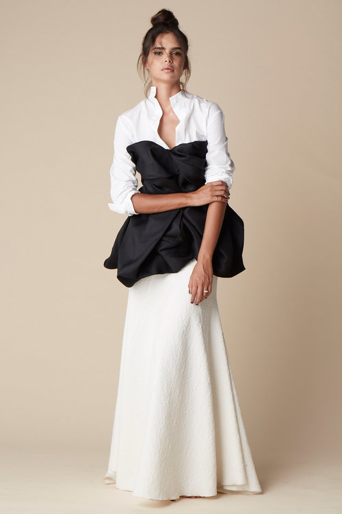 Full shot of a woman in a white button-down shirt, black bodice, and long white textured skirt against a beige background.