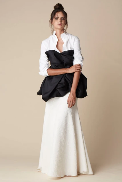 Full shot of a woman in a white button-down shirt, black bodice, and long white textured skirt against a beige background.