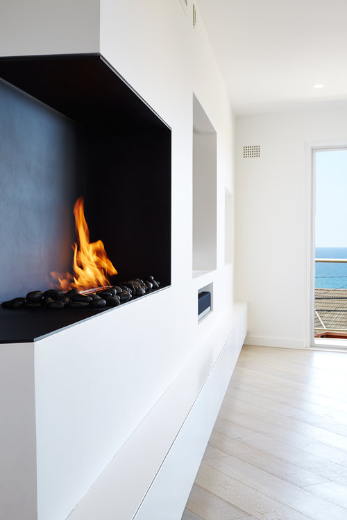 Modern interior featuring a built-in fireplace with flames and decorative stones, set against a backdrop of an ocean view.