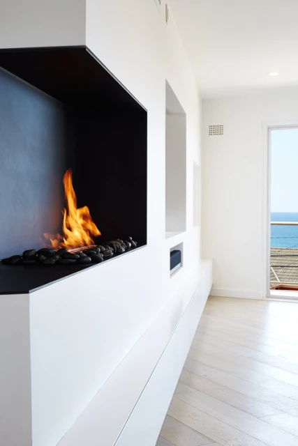 Modern interior featuring a built-in fireplace with flames and decorative stones, set against a backdrop of an ocean view.
