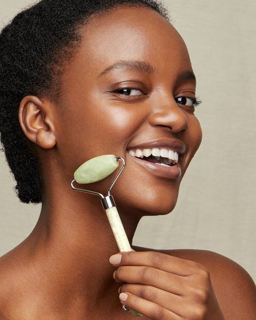 Smiling African American woman uses a jade facial roller on her face in an eye-level shot. Beauty and skincare concept.