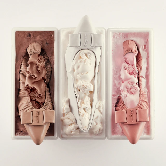 Conceptual shot of three shoe-shaped ice cream scoops in rectangular containers showcasing chocolate, vanilla, and strawberry flavors on white.