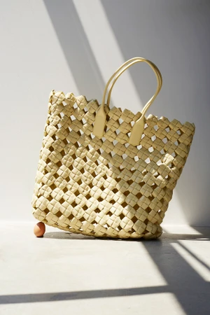 Yellow woven leather tote bag resting on a single raw brown egg against a stark white backdrop.