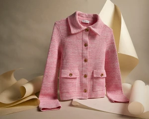 Pink textured knit button-up jacket with front pockets displayed against curved neutral paper backdrop