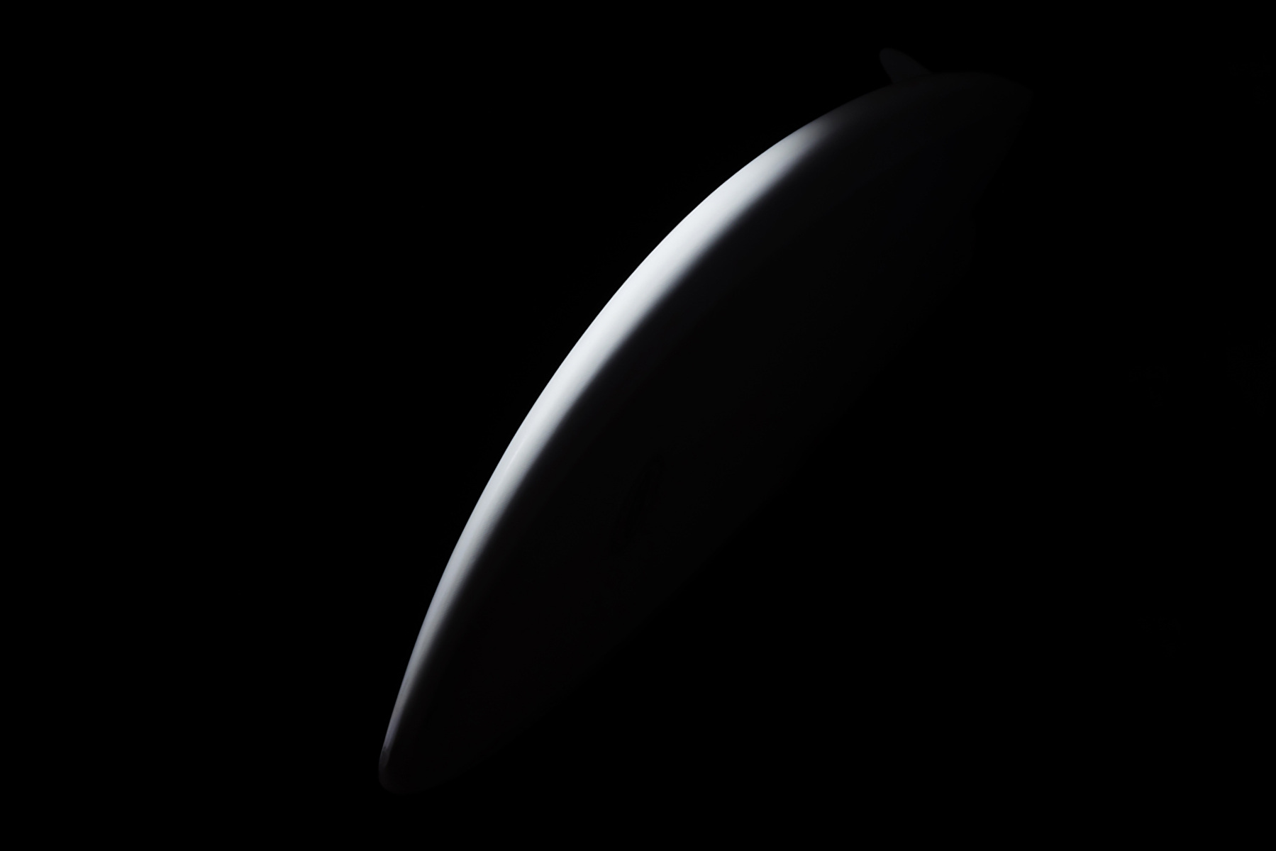 Abstract, minimalist composition showing a curved, white shape against a solid black background with dramatic lighting.