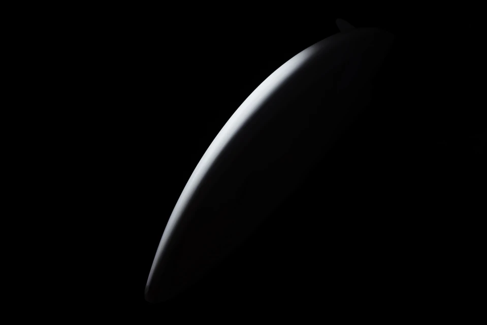 Abstract, minimalist composition showing a curved, white shape against a solid black background with dramatic lighting.