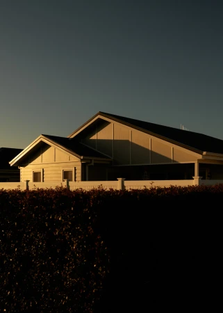 Exterior view of a modern home at sunset featuring clean architectural lines, warm lighting, and a dark hedge in the foreground.