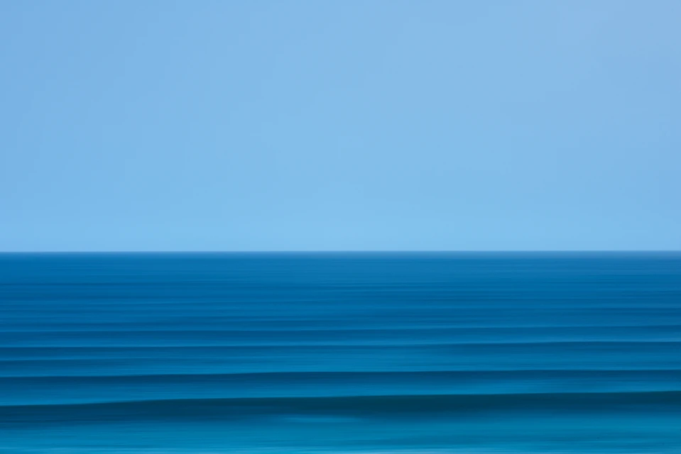 Ocean horizon with clear blue sky and teal waves creating a minimalist, serene seascape in a horizontal, panoramic composition.