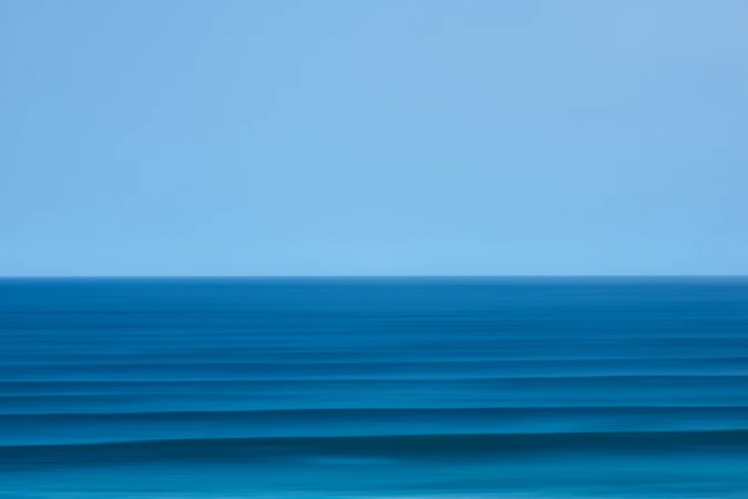 Ocean horizon with clear blue sky and teal waves creating a minimalist, serene seascape in a horizontal, panoramic composition.