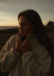 Woman wearing a fleece jacket standing outdoors against a coastline at sunset in Sydney by Alex Brunton