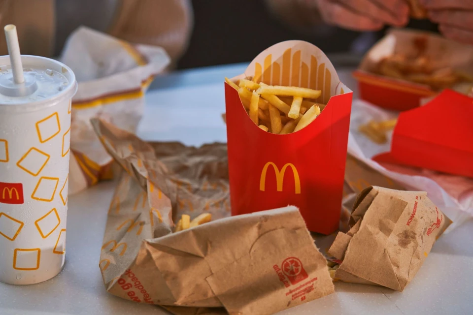 Close-up of McDonald's french fries in a red cardboard container, a drink, and crumpled paper bags on a white surface.
