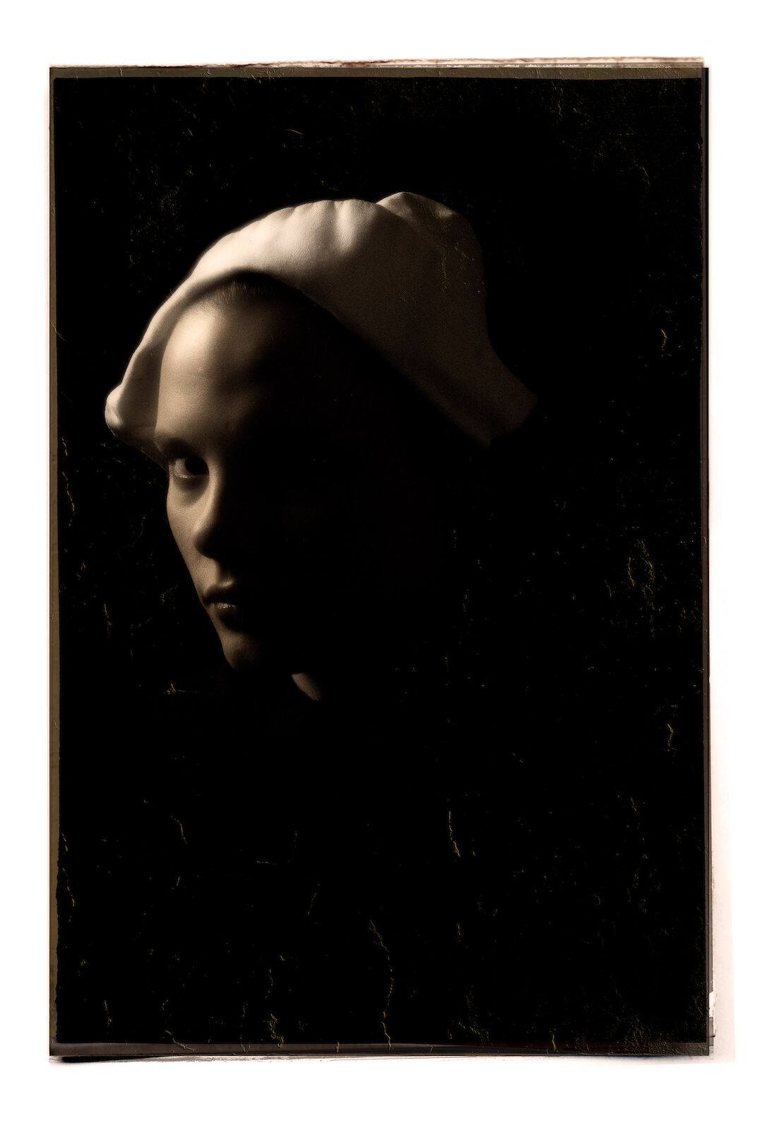 Monochromatic close-up portrait of an adult female with a serious expression wearing a white hat against a dark background.