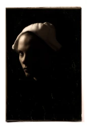 Portrait of a woman wearing a white cap against a dark background in chiaroscuro lighting by Lisa Tomasetti
