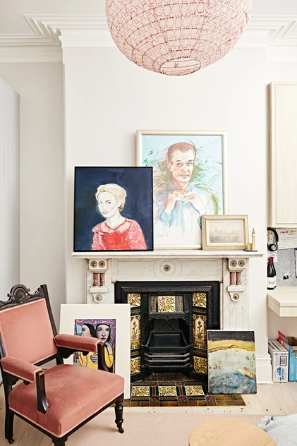Interior view of a living room with artwork displayed above a marble fireplace, illuminated by a decorative hanging light fixture.