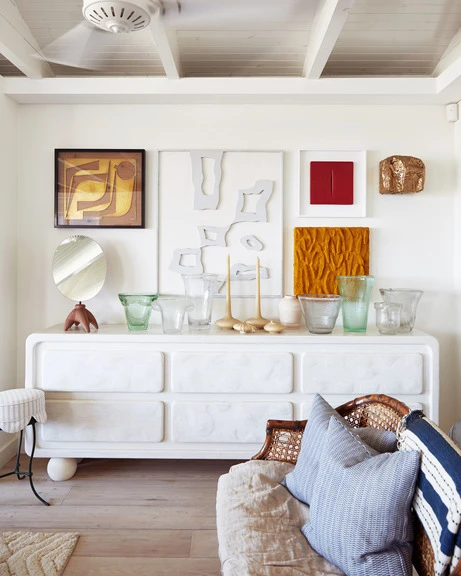 Bright living room interior with white dresser topped by vases and artwork, set against a white wall with a ceiling fan.