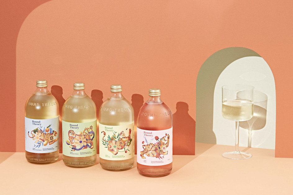 Four bottles of Bound Theory beverages with tiger illustrations, placed against a peach-colored wall, complemented by glasses and a geometric arch.