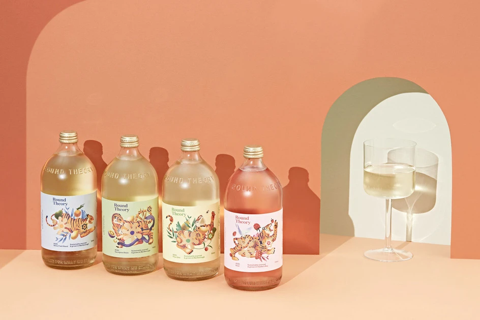 Four bottles of Bound Theory beverages with tiger illustrations, placed against a peach-colored wall, complemented by glasses and a geometric arch.