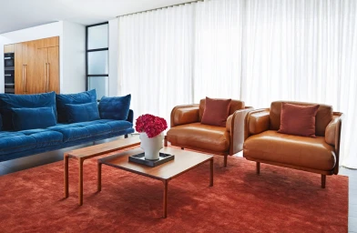 Modern living room interior with a blue velvet sofa, two brown leather armchairs, and a square wooden coffee table.