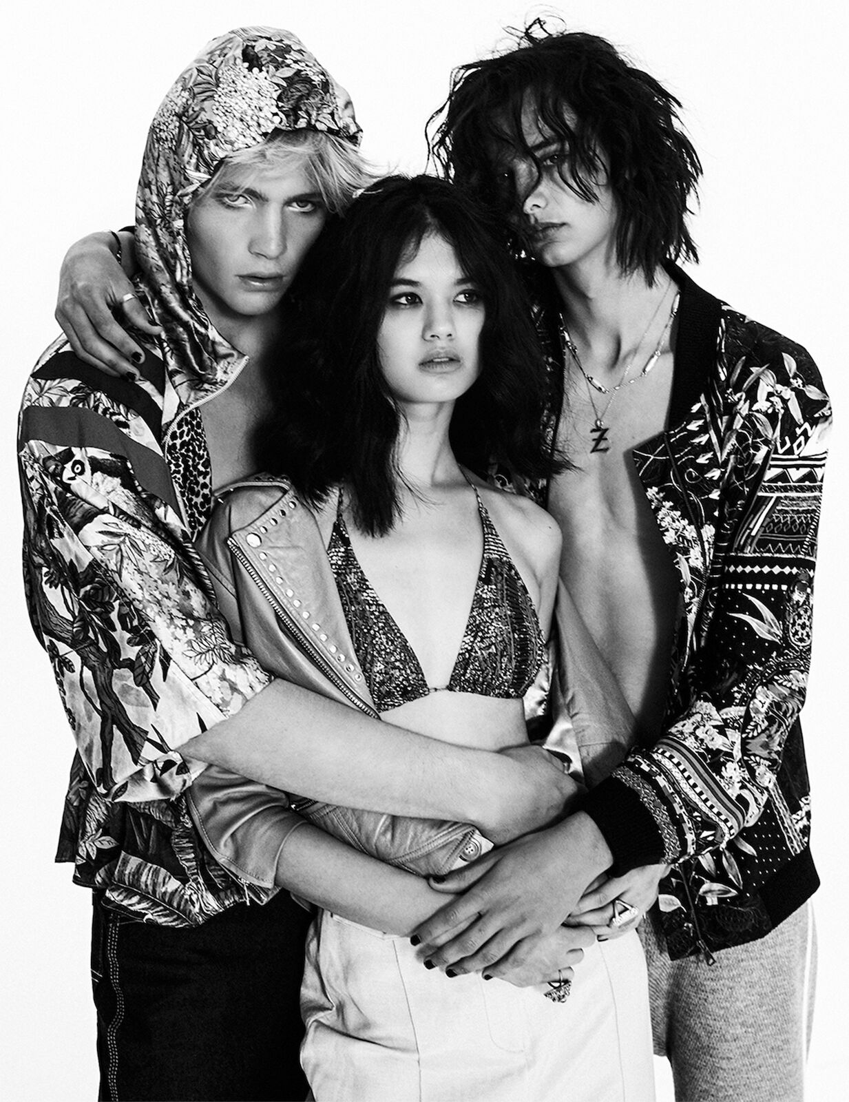 Black and white fashion shot of three models in a studio setting, featuring diverse clothing styles and poses against a white backdrop.