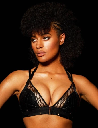 Portrait of a woman with dark curly hair, wearing a black bra with netting details against a dark background in a studio shot.