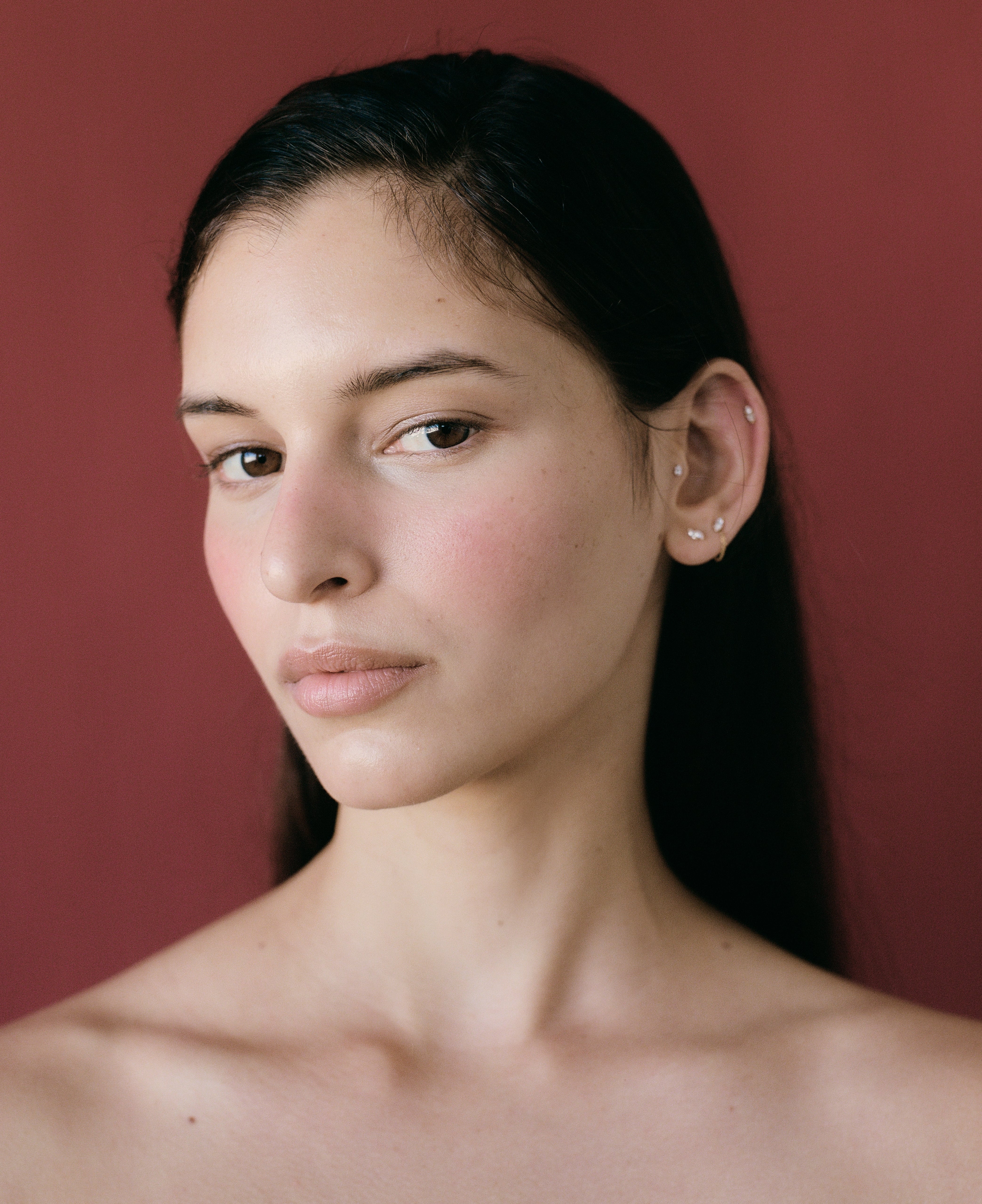 Portrait of a brunette woman with fair skin against a reddish-brown background in a beauty-style photograph with natural lighting.