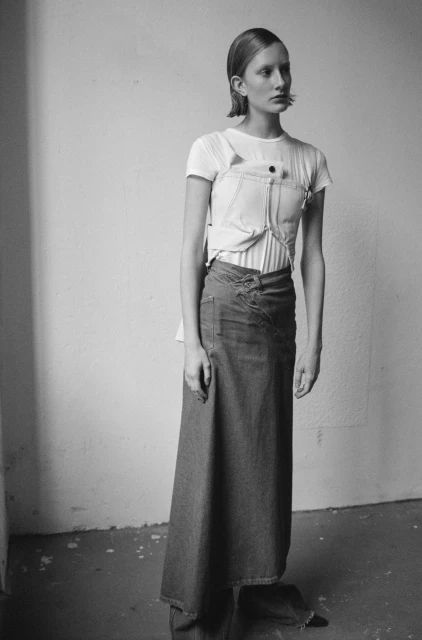 A model poses indoors in a white tee shirt with a deconstructed denim top and a long denim skirt in a black and white fashion shot.