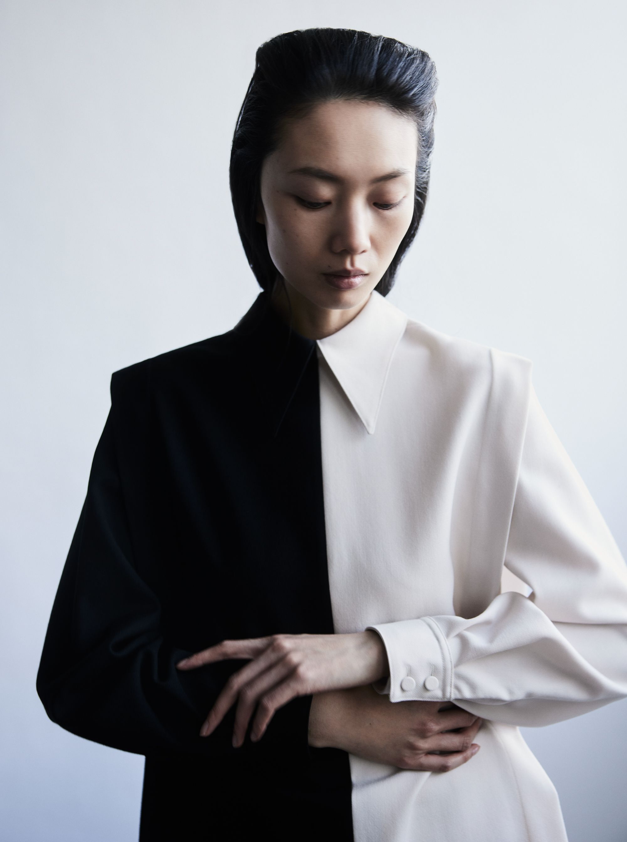 Elegant Asian woman in black-and-white dress, posing indoors with folded hands. Stylish color-block fashion in a studio setting.